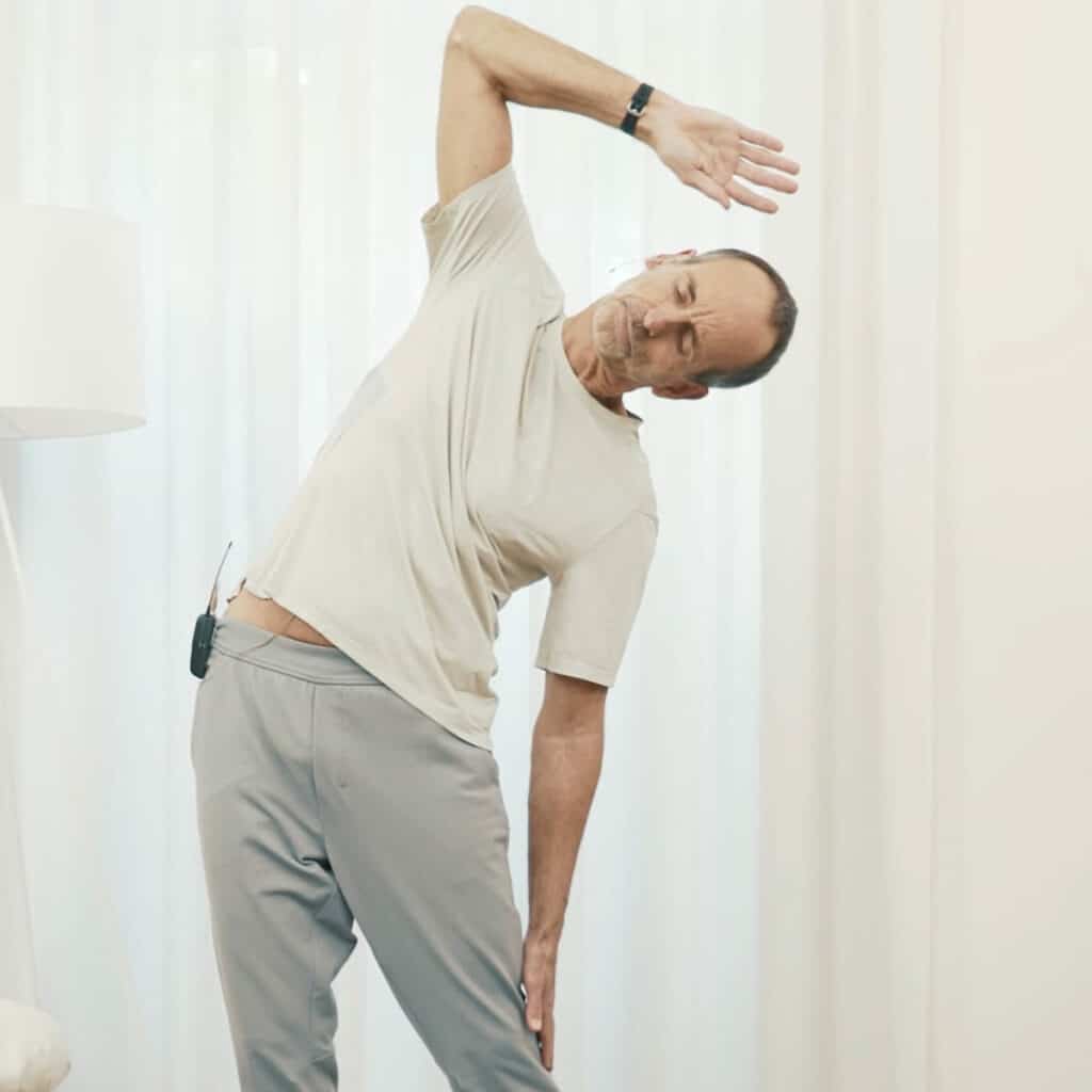 Schmerzspezialist Roland Liebscher-Bracht steht hüftbreit. Seinen Oberkörper neigt er zur Seite und lässt dabei seinen linken Arm an seinem Oberschenkel liegen. Seinen rechten Arm hebt er über seinen Kopf.