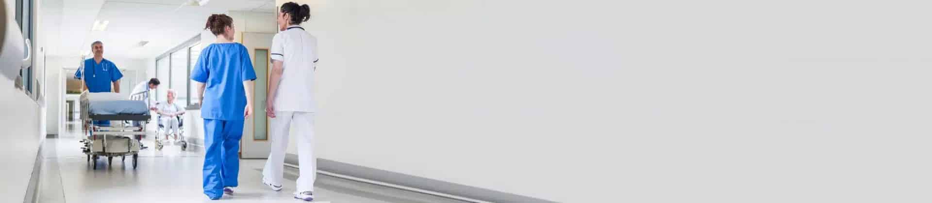 Pfleger schiebt Krankenhausbett durch Flur, Ärztinnen kommen ihm entgegen