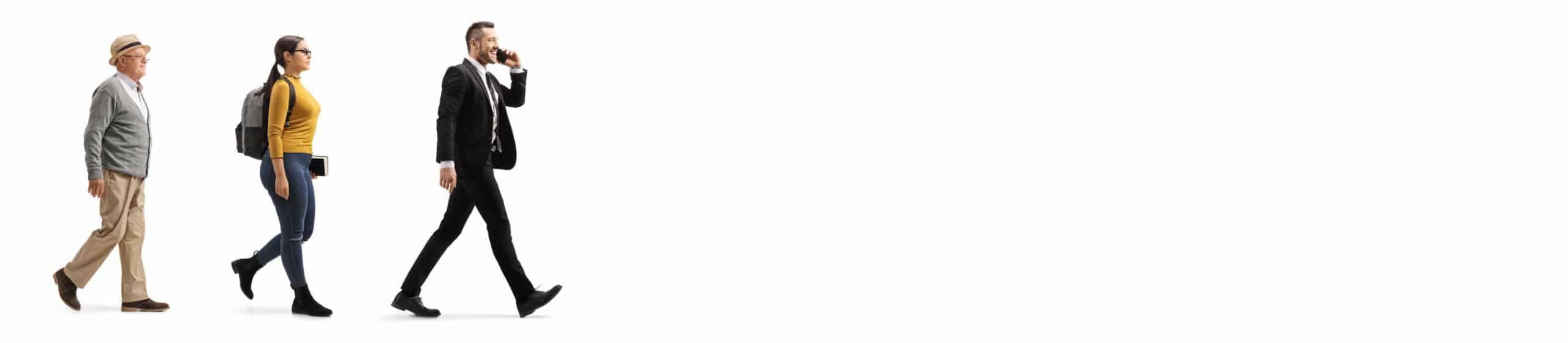 ein älterer Mann, eine jüngere Frau und ein mittelalter Mann im Anzug laufen hintereinander entlang