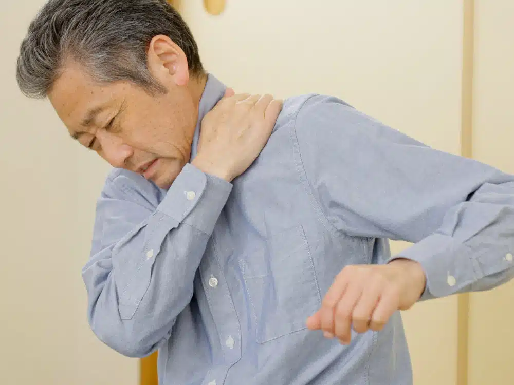 Ein Mann greift sich mit schmerzverzerrtem Gesicht mit Hand an den Nacken