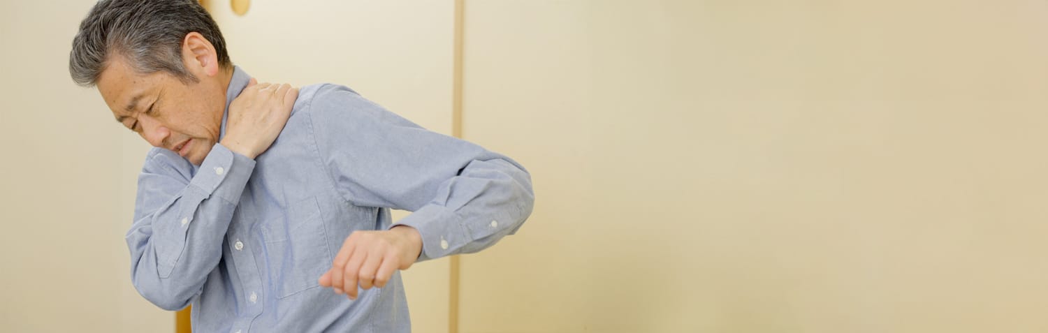 Ein Mann greift sich mit schmerzverzerrtem Gesicht mit Hand an den Nacken