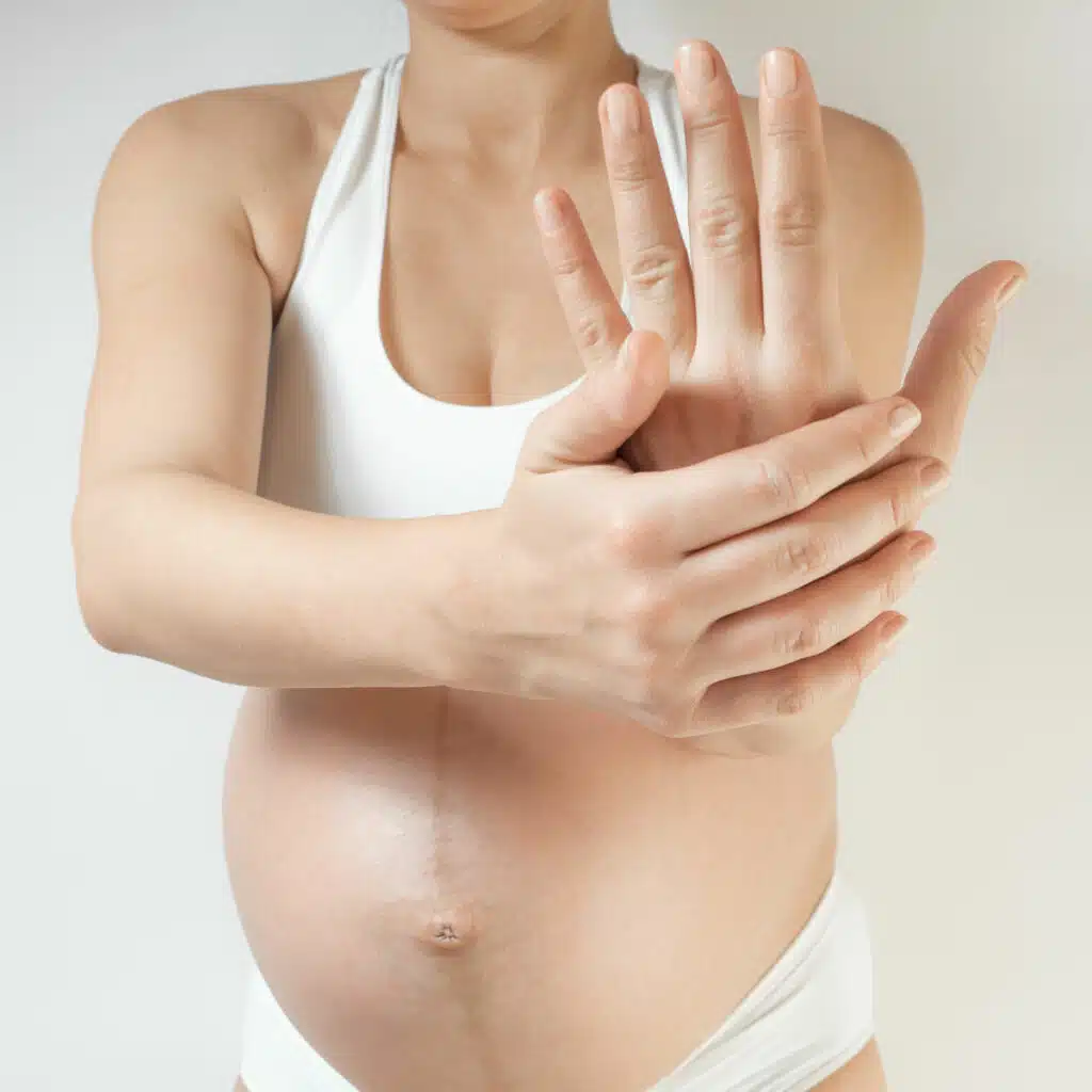 Eine Schwangere hält ihre Hand frontal in die Kamera. Sie hat die Hand aufgerichtet, sodass der Handrücken zum Betrachter zeigt. Mit der anderen Hand umgreift sie das Handgelenk.