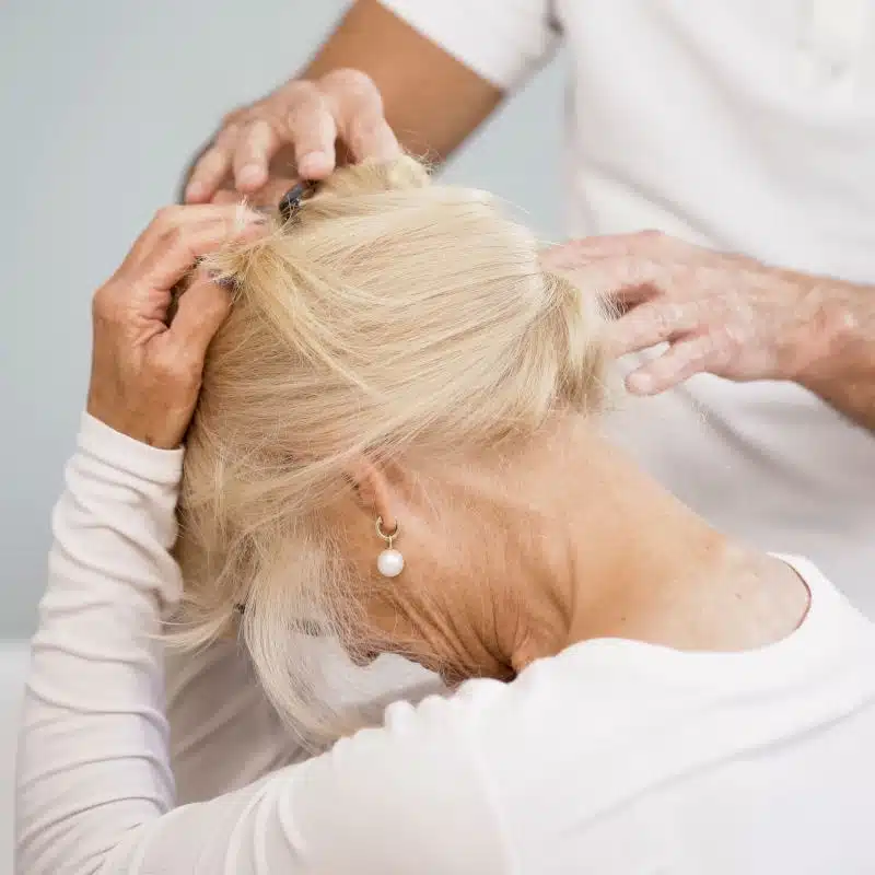 Eine blonde Frau greift sich mit beiden Händen an den Kopf und zieht ihn nach vorne zur Brust.