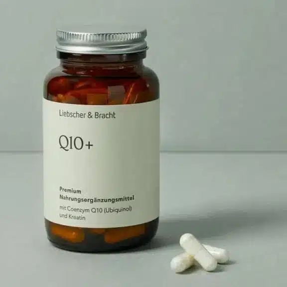 Ein braunes Glasfläschchen steht vor einem olivgrünen Hintergrund. Es ist mit Q10plus beschriftet. Davor liegen drei weiße Pillen.