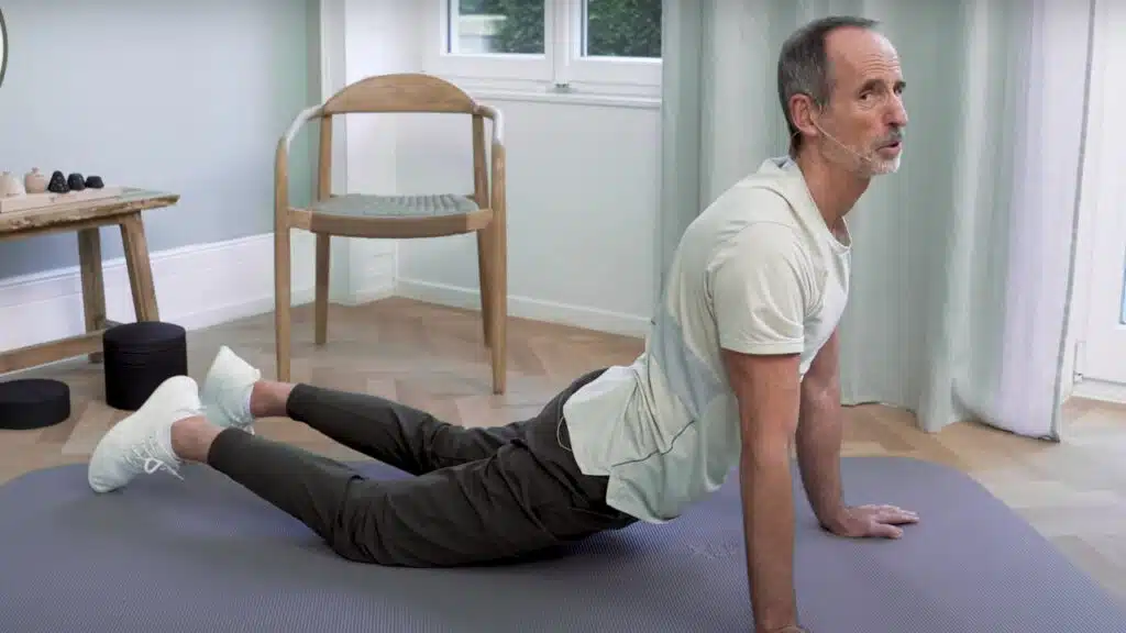 Roland Liebscher-Bracht macht eine Dehnübung zur Dehnung der Hüftbeuger. Er lässt sein Becken durchhängen und stützt sich mit den Armen vorne ab. Die Beine liegen nach hinten ausgestreckt.