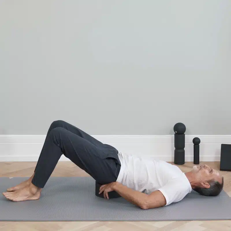 Roland Liebscher-Bracht liegt am Boden und platziert einen Rückenretter unter seinem Kreuzbein.