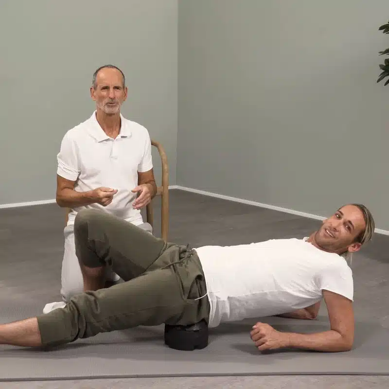 Roland Liebscher-Bracht kniet neben einem Mann, der vor ihm auf dem ISG-Ischias-Retter liegt.