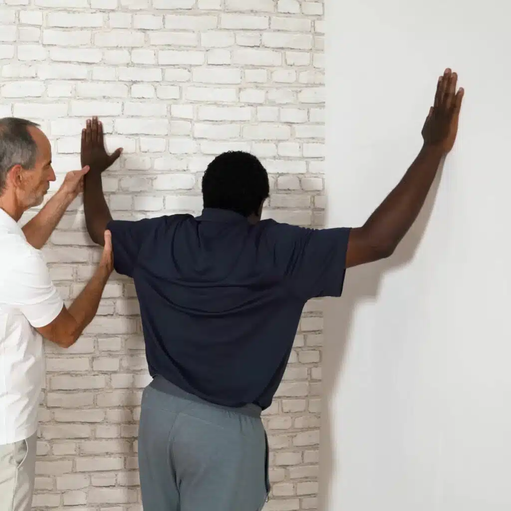 Eine Person steht mit angewinkelten und angehobenen Armen in einer Raumecke.