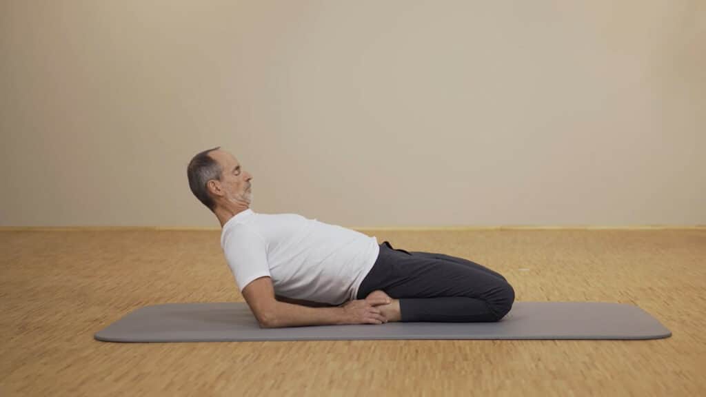 Roland Liebscher-Bracht liegt im weißen Shirt auf einer Übungsmatte und führt eine Dehnung am vorderen Oberschenkel durch