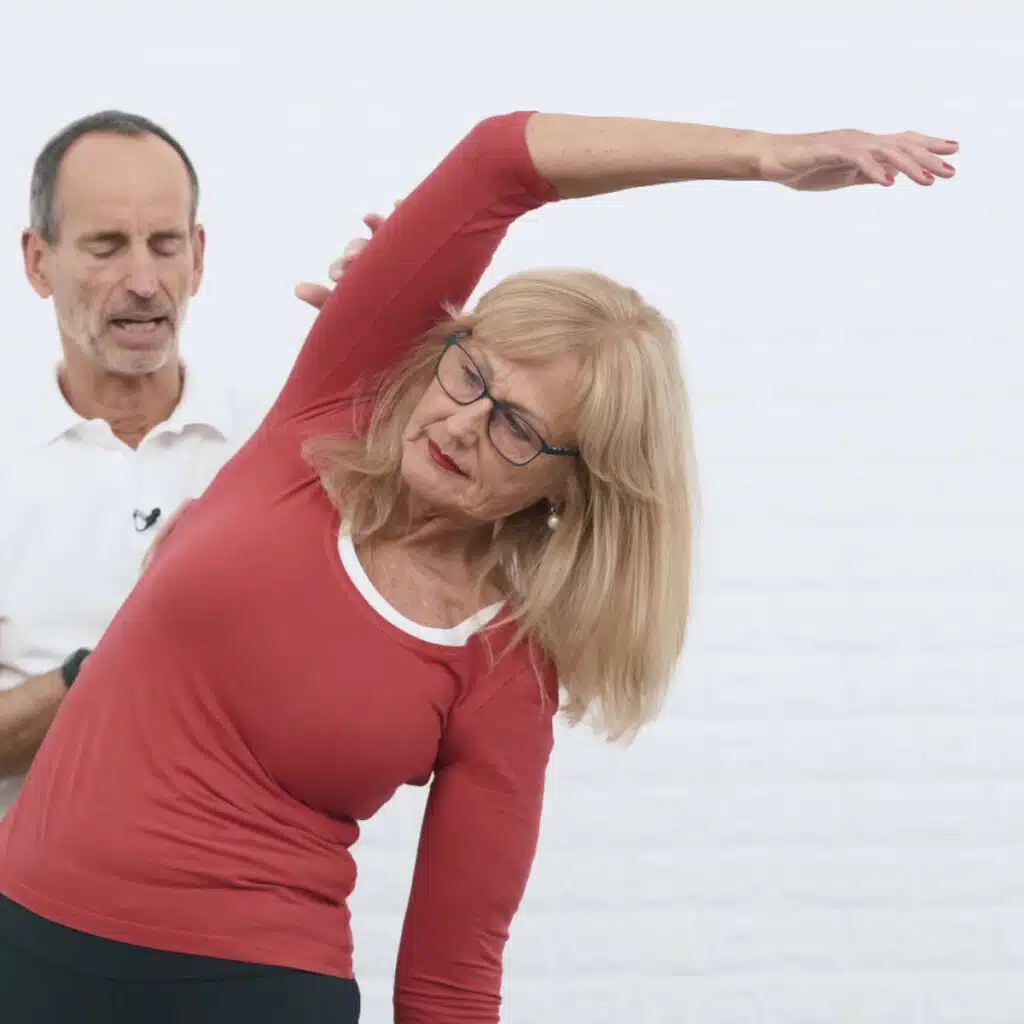 Eine Person hat den rechten Arm angehoben und neigt den Oberkörper nach links. Der rechte Arm zieht über ihrem Kopf nach links.