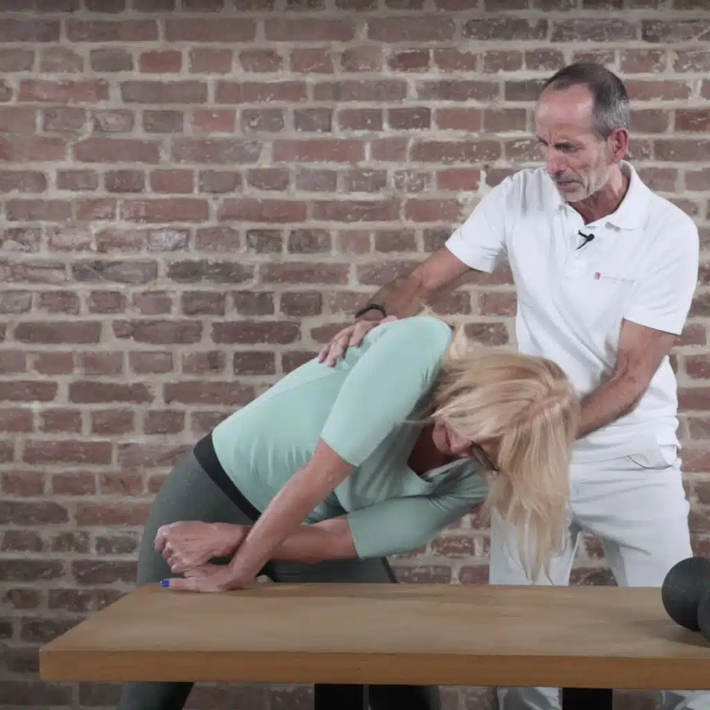 Die Patientin hat die rechte Hand zu sich gedreht, sodass der Unterarm gedehnt wird. Mit der linken Hand zieht sie die Finger der rechten Hand etwas nach oben, um die Dehnung zu verstärken. Zusätzlich lehnt sie sich weit nach links und versucht den Oberkörper auf einem Tisch abzulegen.