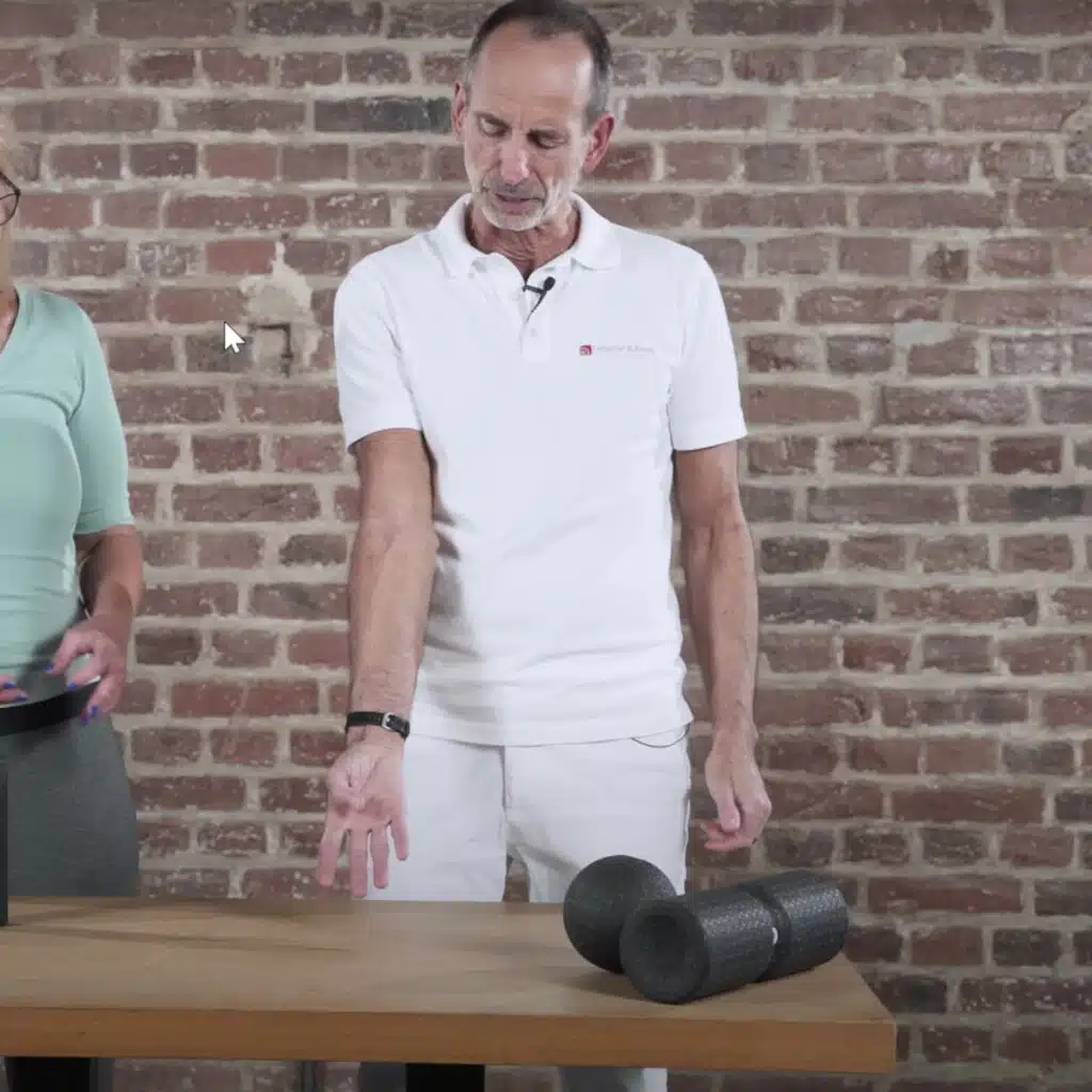 Eine Person steht vor einem Tisch und streckt ihren rechten Arm so aus, dass die Handfläche nach oben zeigt. Sie legt den Daumen in die Handfläche.