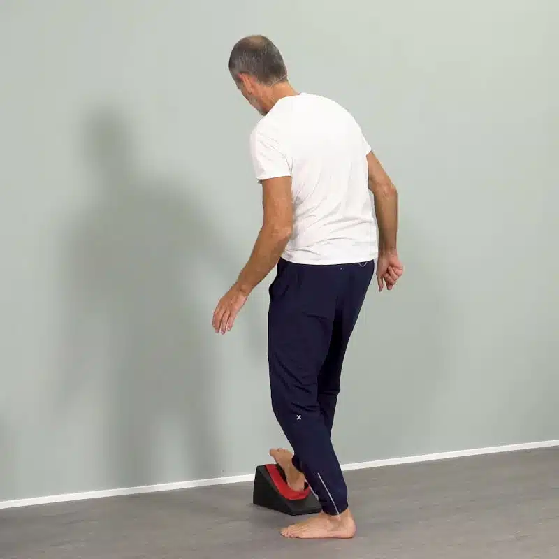 Ein Mann steht in Schrittstellung vor einer hellgrauen Wand und platziert seinen rechten Fuß auf dem Knieretter von Liebscher & Bracht.