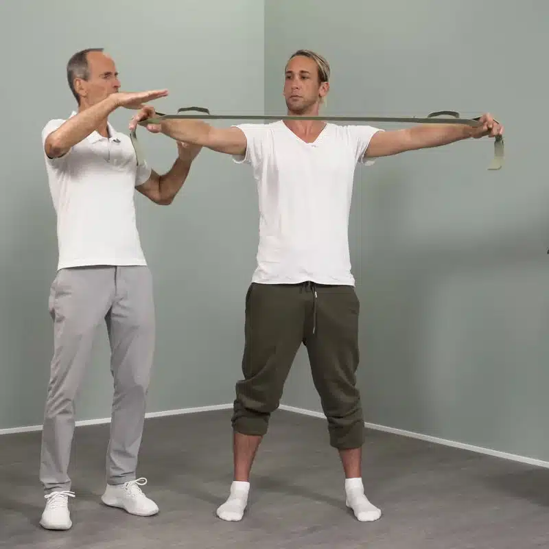 Ein junger Mann hat seine Arme seitlich ausgestreckt und hält mit beiden Händen den Schulterretter von Liebscher & Bracht vor seinen Körper.