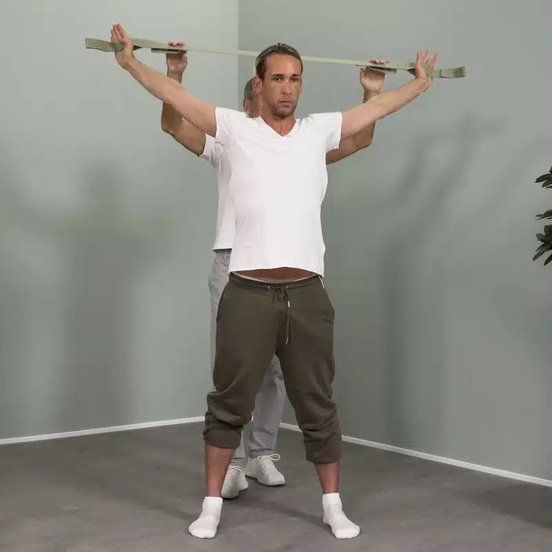 Ein junger Mann hat seine Arme seitlich nach oben ausgestreckt und hält mit beiden Händen den Schulterretter von Liebscher & Bracht.