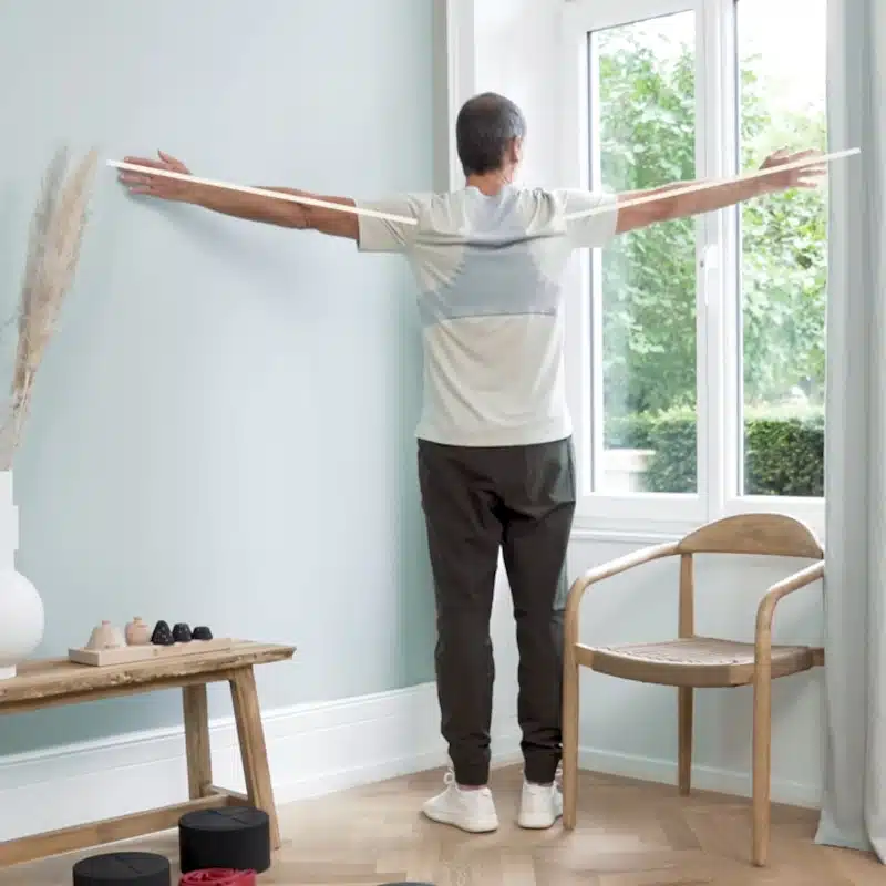 Roland Liebscher-Bracht steht mit ausgebreiteten Armen in einer Raumecke, um eine Dehnung für den Brustkorb durchzuführen