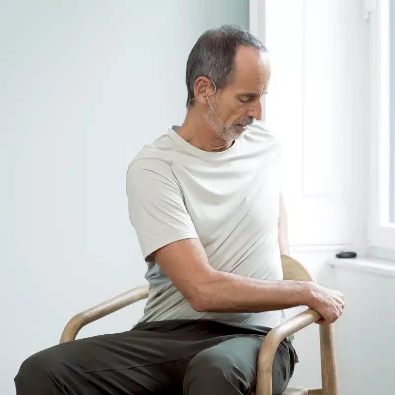 Roland Liebscher-Bracht sitzt auf einem Stuhl und dreht sich weit nach links, um eine Dehnung bei BWS-Syndrom durchzuführen