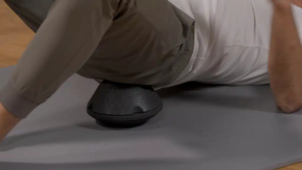 Eine Person liegt mit dem linken Gesäß auf dem ISG-Ischias-Retter von Liebscher und Bracht. Die Füße und die Ellenbogen sind am Boden aufgestellt.