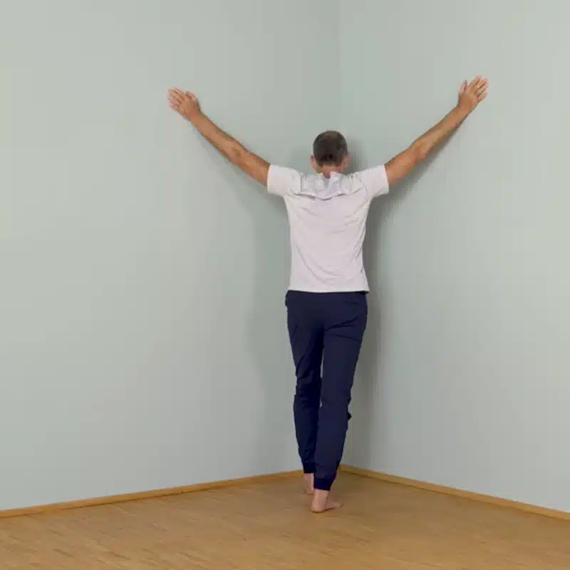 Roland steht in einer Zimmerecke und führt die Brustöffnung bei Schulterschmerzen aus