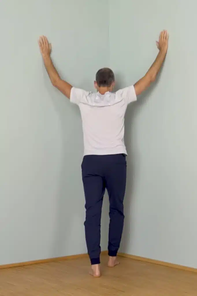 Roland steht in einer Zimmerecke und führt die Brustöffnung bei Schulterschmerzen aus