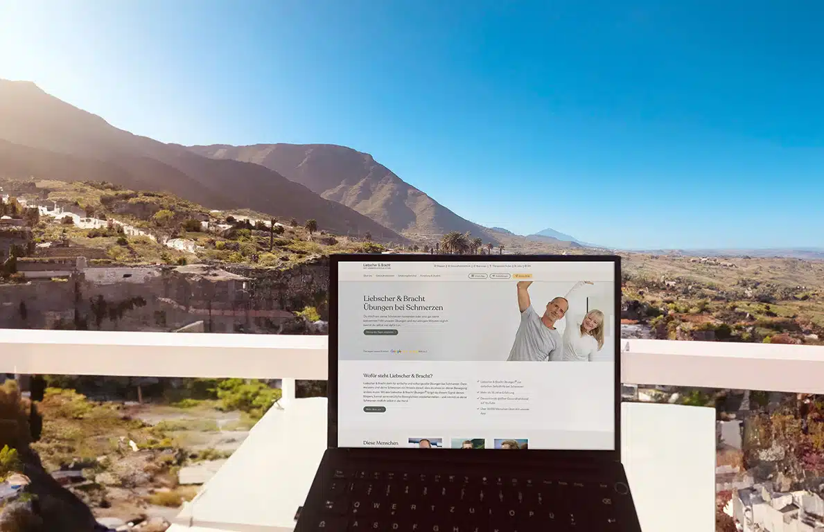 Ein Laptop mit einer aufgerufenen Lisbscher & Bracht-Website steht auf einem Tisch. Im Hintergrund ein strahlend blauer Himmel und der Blick auf gebirgiges Gelände