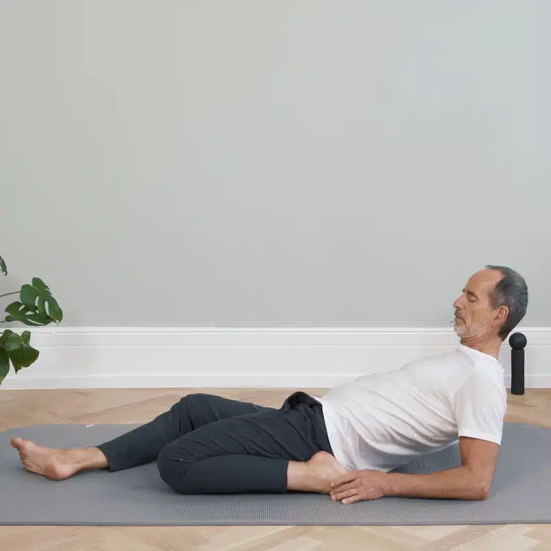 Roland Liebscher-Bracht liegt mit aufgestellten Ellenbogen am Boden. Er hat ein Bein ausgestreckt. Das andere Bein ist angewinkelt und der Fuß liegt neben seinem Gesäß.