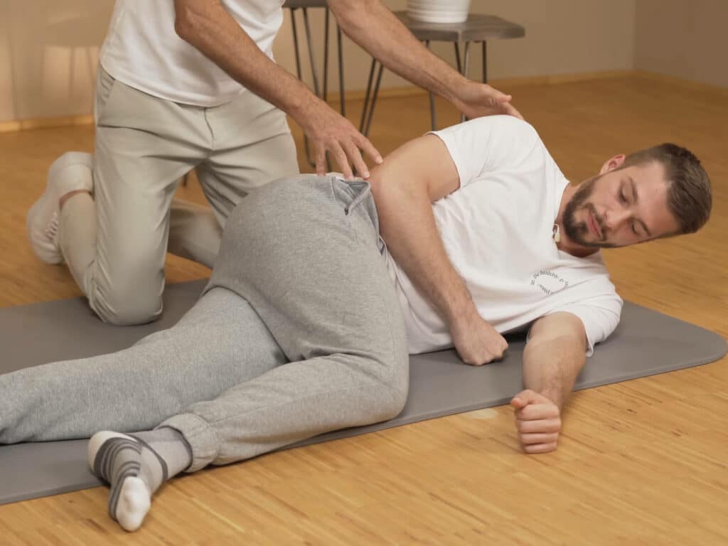 Ein Mann liegt am Boden und dreht sich vom Rücken auf die Seite, indem er sein rechtes Bein über das linke Bein schlägt.