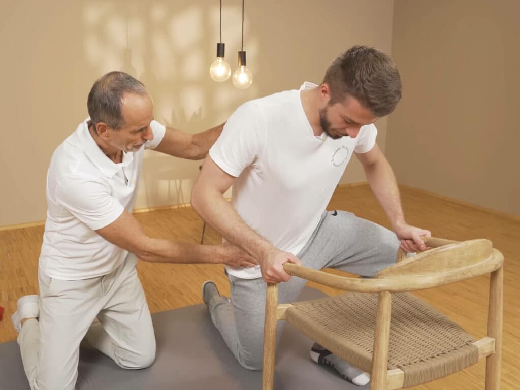 Ein Mann stützt sich mit beiden Armen an einem Stuhl ab, um aufzustehen.