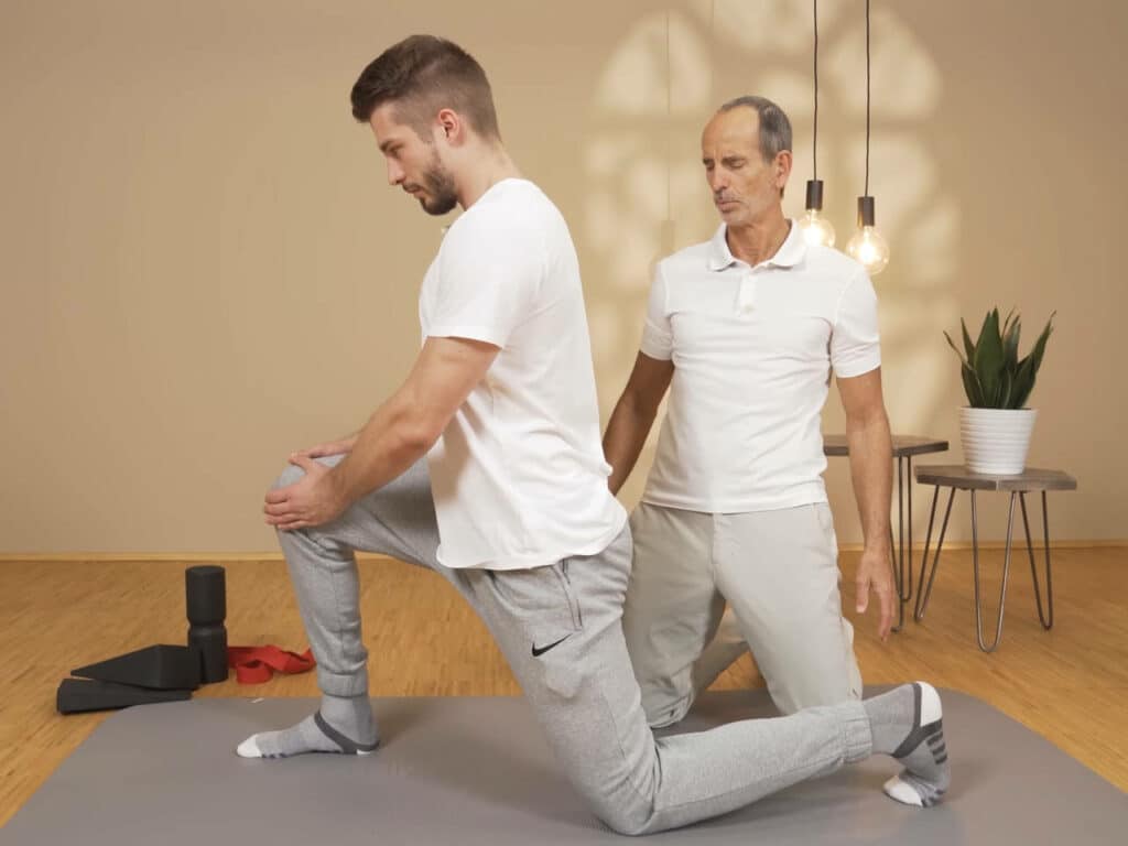 Ein Mann kniet mit einem Bein am Boden, hat das andere Bein aufgestellt und bewegt seine Hüfte nach vorne, um eine Dehnung zu erreichen.