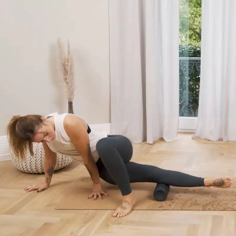 Eine Frau macht am Boden eine Faszien-Rollmassage und hat dazu ihren linken Unterschenkel mittig auf der Faszienrolle platziert.