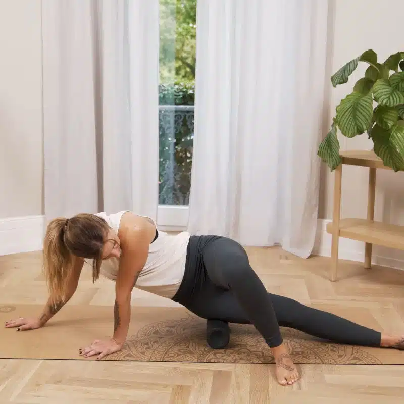 Für eine Faszien-Rollmassage hat sich eine Frau seitlich auf den Boden begeben und bewegt ihren Oberschenkel über eine Faszienrolle.