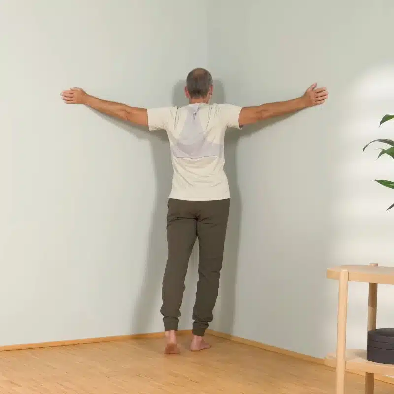 Roland Liebscher-Bracht steht mit seitlich ausgestreckten Armen in einer Raumecke.