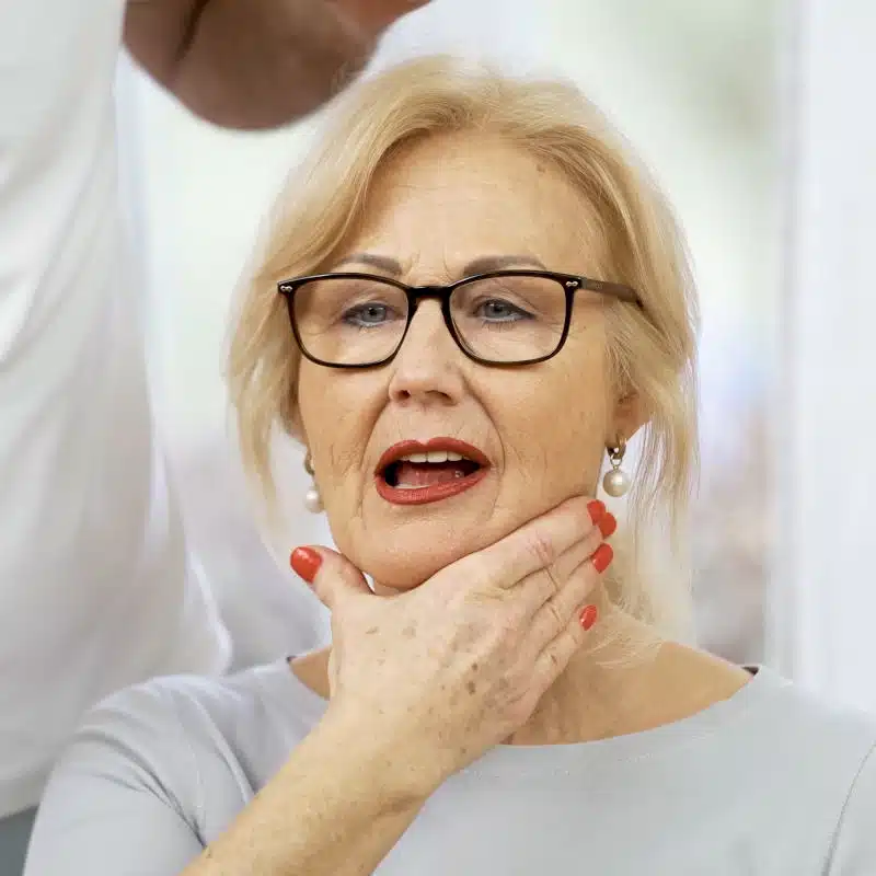 Eine Frau hält ihre linke Hand an die rechte Seite des Unterkiefers.