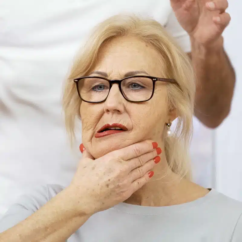 Eine Frau schiebt mit der linken Hand ihren Unterkiefer weit nach links.