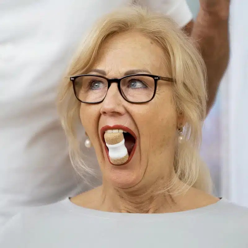 Eine Frau hat ihren Mund weit geöffnet und zwischen ihren Schneidezähnen steckt der Kieferretter von Liebscher & Bracht.