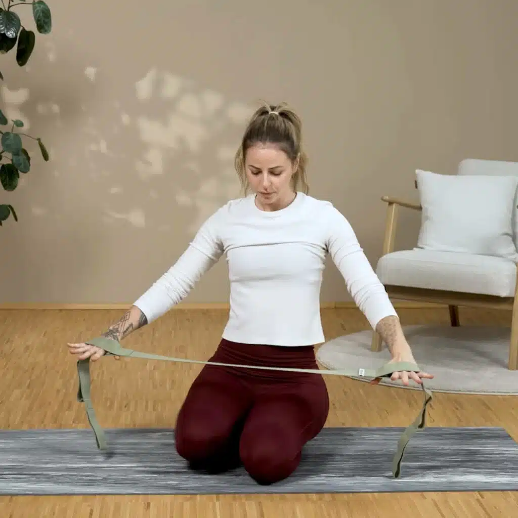 Eine Person hält den Schulterretter in den Händen und fädelt ihre Hände rechts und links in die Schlaufen ein. Sie hat die Arme vor dem Körper und unten. So bereitet sie die Übung vor.