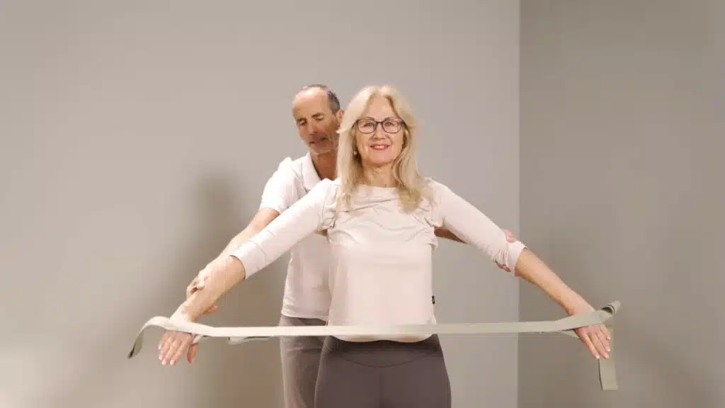 Eine Person hat die Arme weit geöffnet und die Hände durch die Schlaufen des Schulterretters gesteckt. Die Arme sind gestreckt.