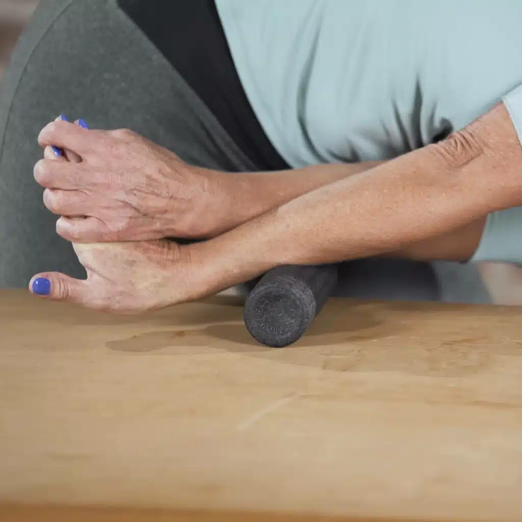Das Bild zeigt eine Faszien-Rollmassage am Unterarm. Dazu hat die ausführende Person eine Hand angewinkelt, den zugehörigen Arm gestreckt und rollt mit dem Unterarm über eine kleine schwarze Faszienrolle.