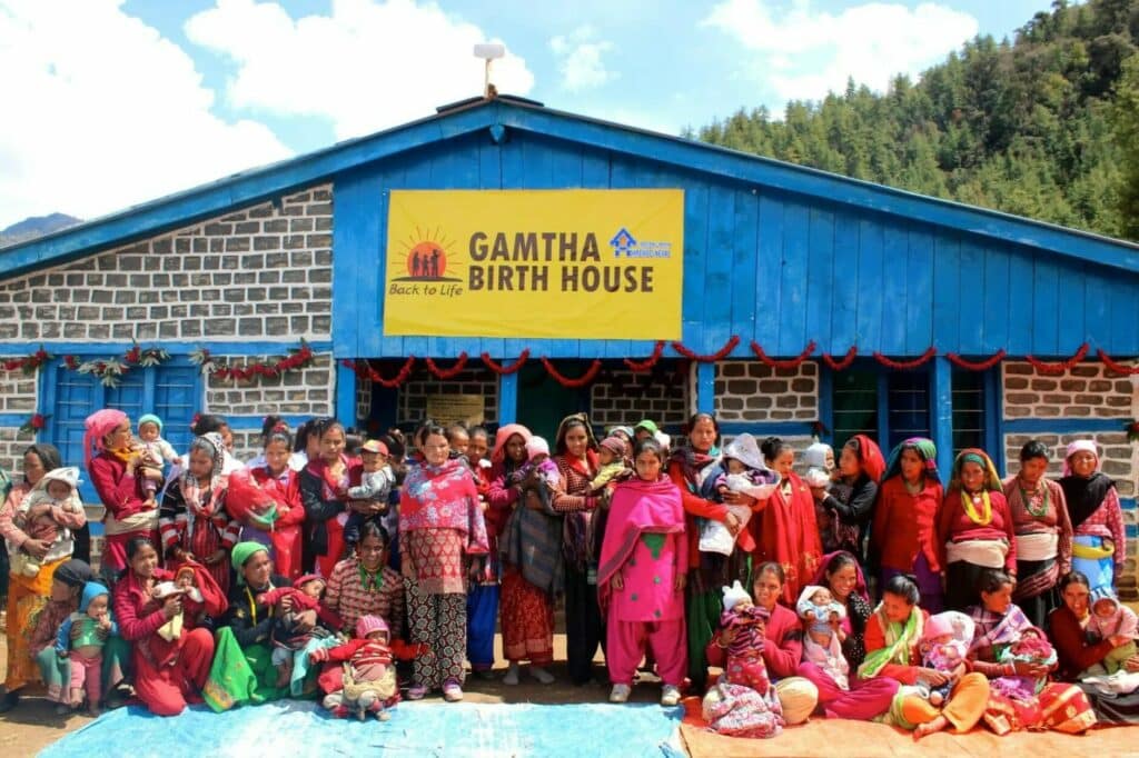 Eine Gruppe nepalesischer Frauen mit ihren Kindern und Säugliingen vor einem Geburtshaus