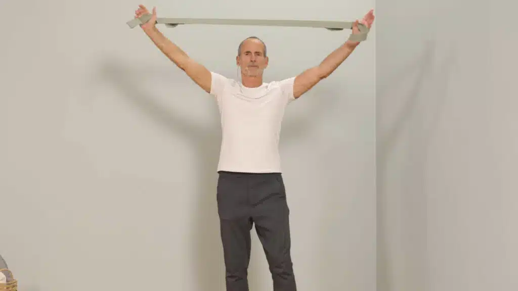 Eine Person hat beide Hände in den Schlaufen des Schulterretters eingefädelt. Sie streckt die Arme weit über den Kopf, die Arme sind gestreckt und der Schulterretter ist auf Spannung gebracht.