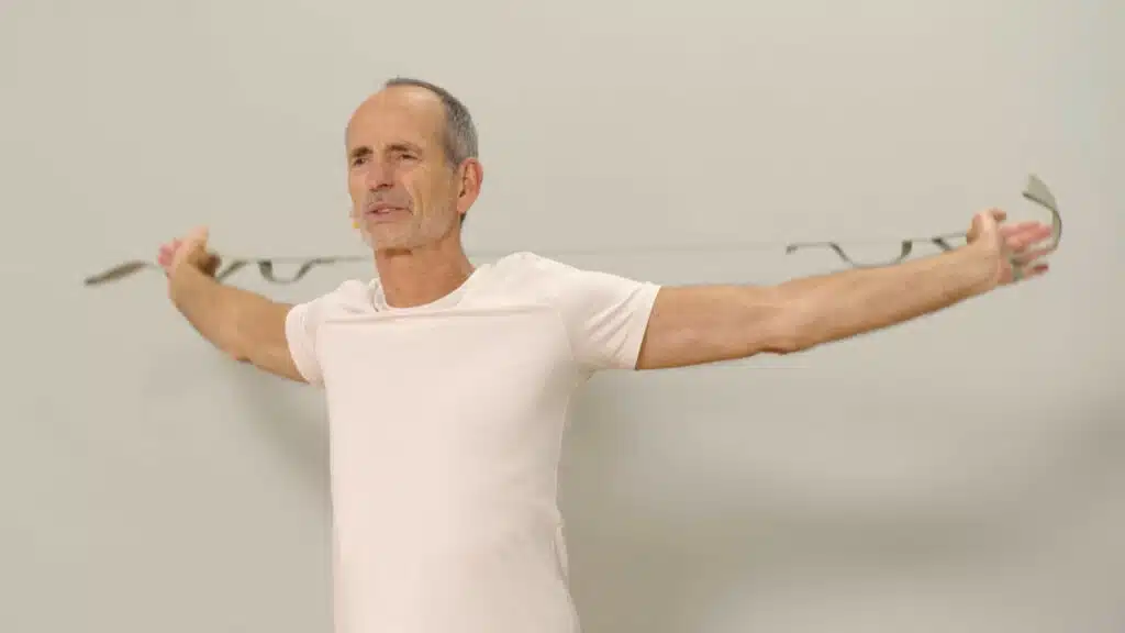 Eine Person hat beide Hände in den Schlaufen des Schulterretters eingefädelt. Sie streckt die Arme weit nach hinten hinter den Körper, die Arme sind gestreckt und der Schulterretter ist auf Spannung gebracht.