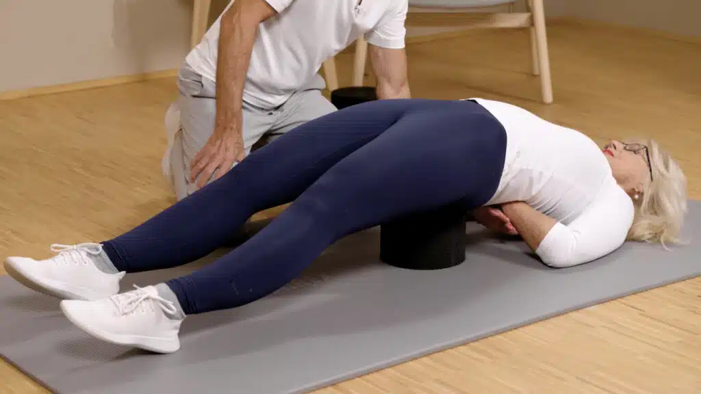 Eine Frau liegt auf dem Rückenretter von Liebscher & Bracht und dehnt ihre Hüftbeuger-Muskeln.