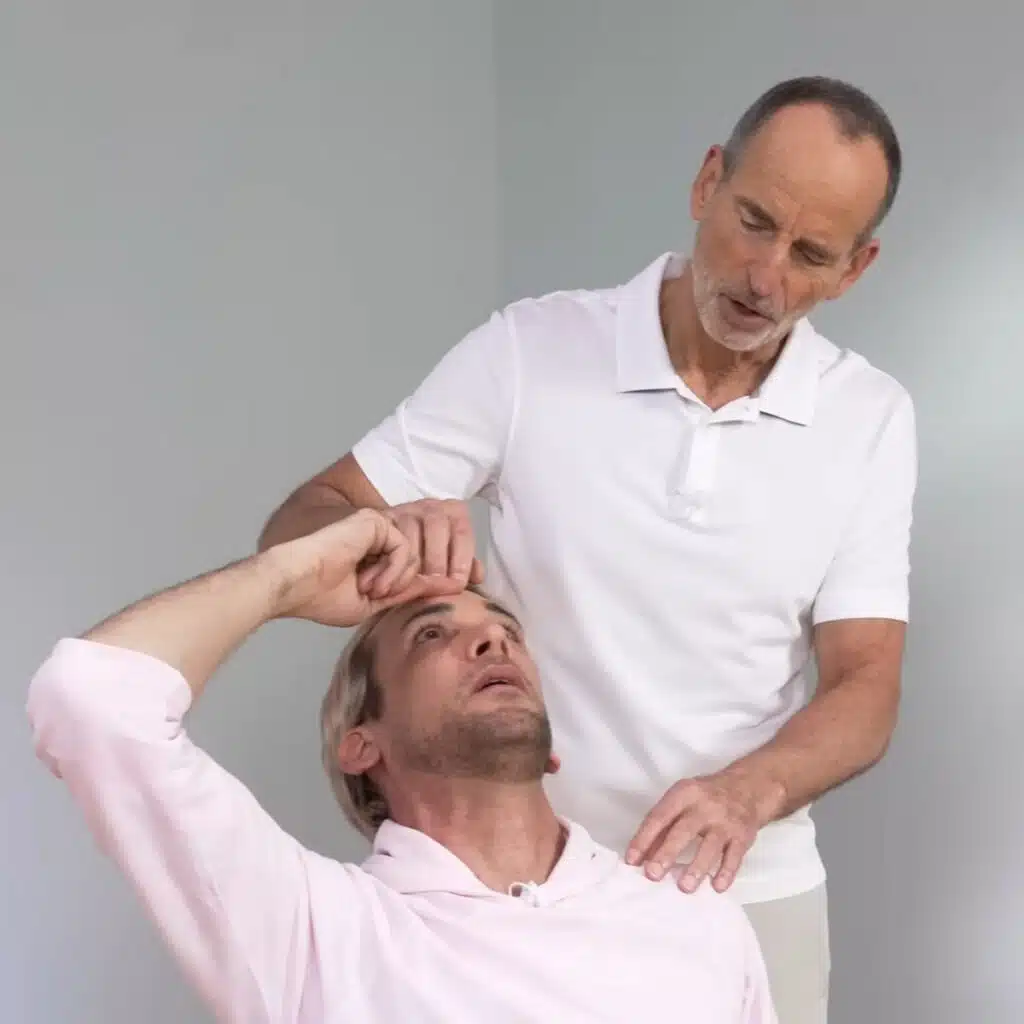 Eine Person hat den rechten Zeigefinger auf der Stirn abgelegt. Sie neigt den Kopf weit zurück.