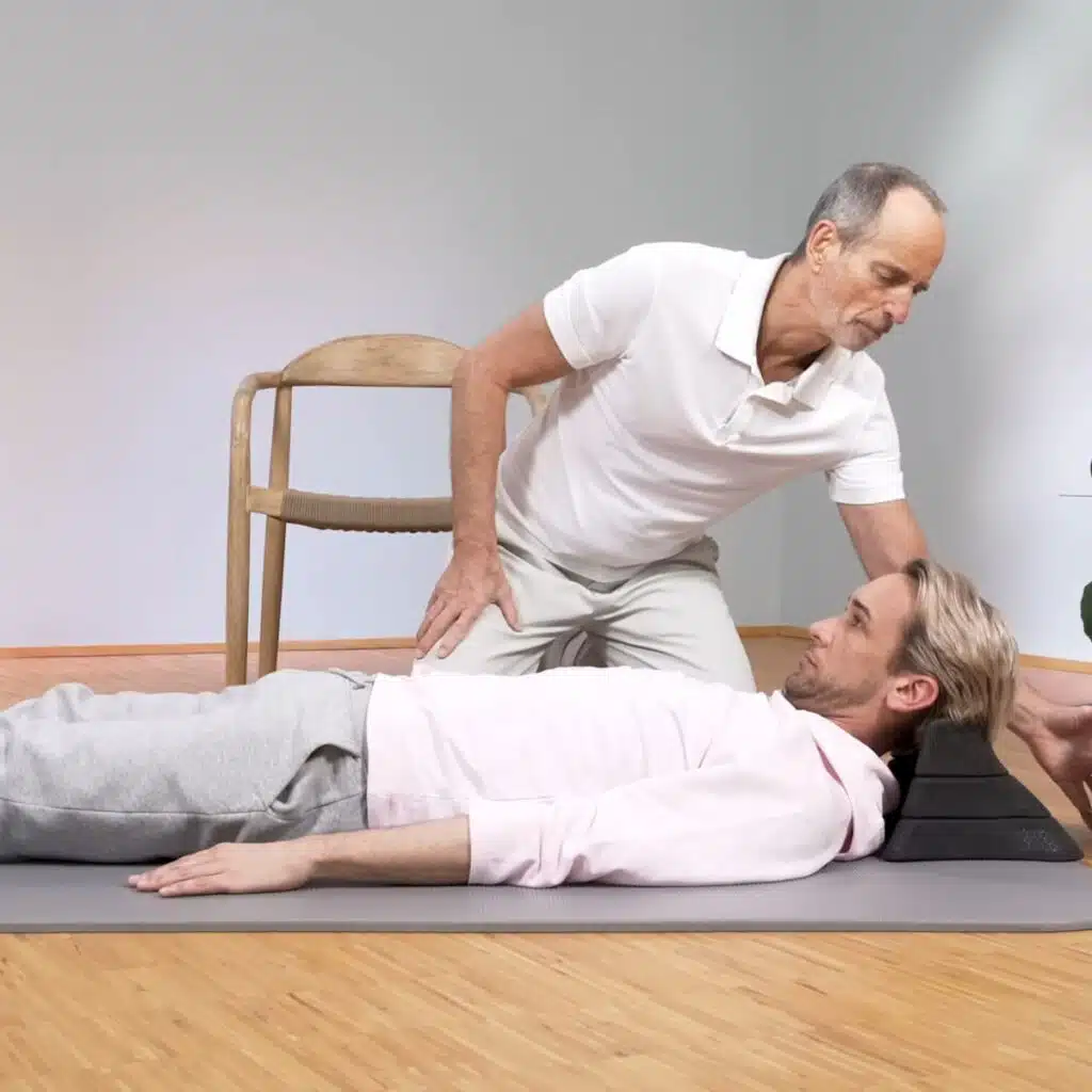 Eine Person liegt am Boden und hat den Kopf auf dem Nackenretter abgelegt. Das Kinn zieht zum Brustkorb.