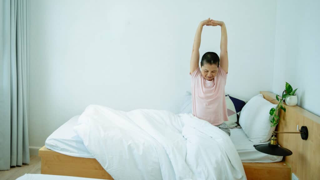 Eine Person sitzt im Bett und streckt sich ausgiebig.