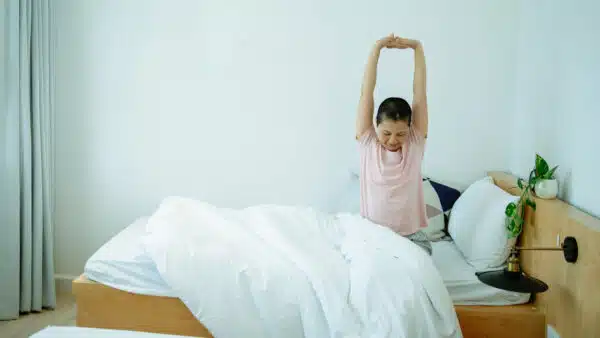 Eine Person sitzt im Bett und streckt sich ausgiebig.