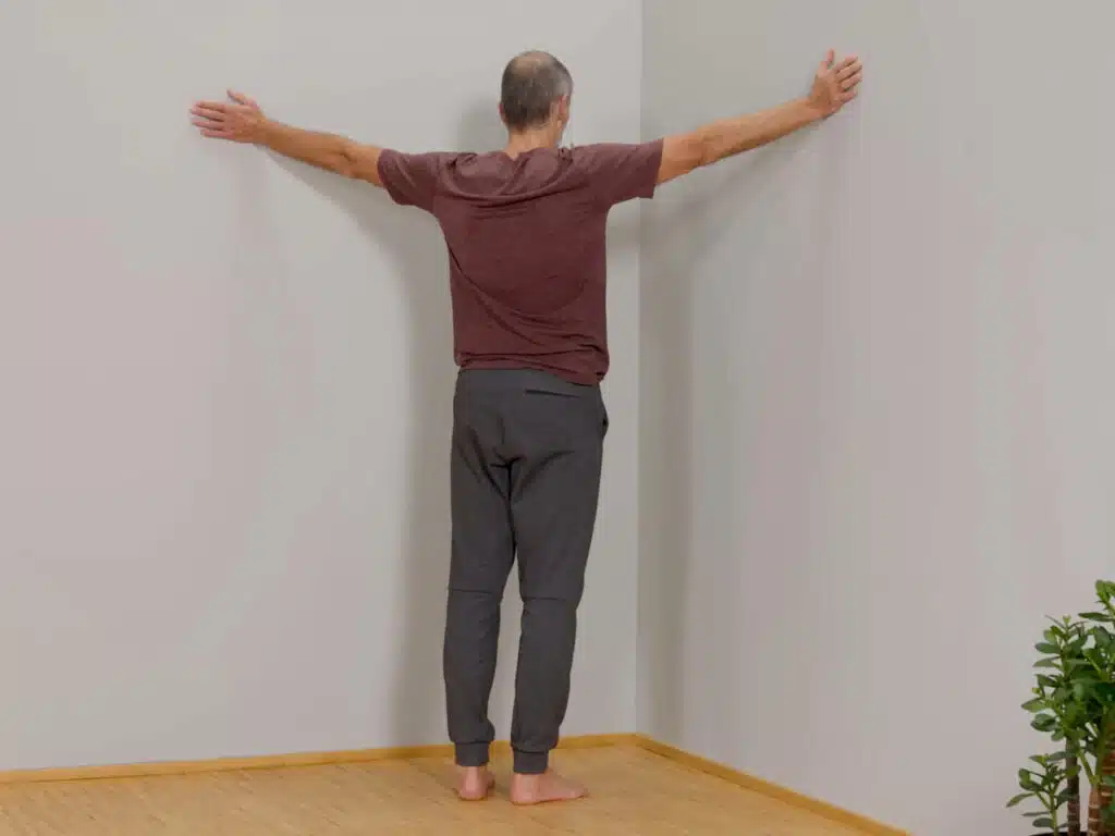 Ein Mann steht vor einer Raumecke und hat seine Arme zu beiden Seiten ausgestreckt.