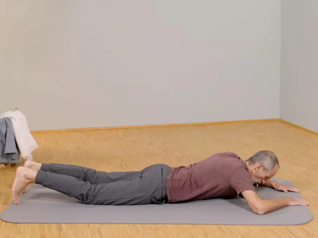 Roland Liebscher-Bracht liegt bäuchlings auf einer Übungsmatte und hat seine Arme vor sich am Boden abgelegt.