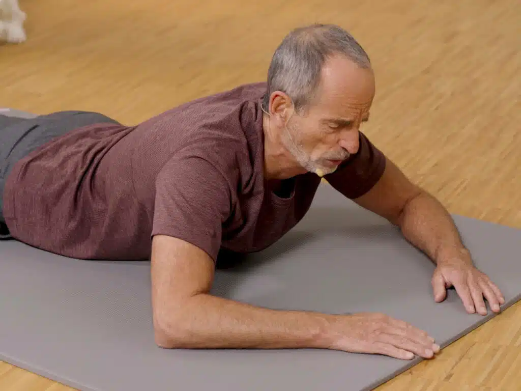 Roland Liebscher-Bracht liegt bäuchlings am Boden und hat seinen Brustkorb für eine Dehnübung angehoben.