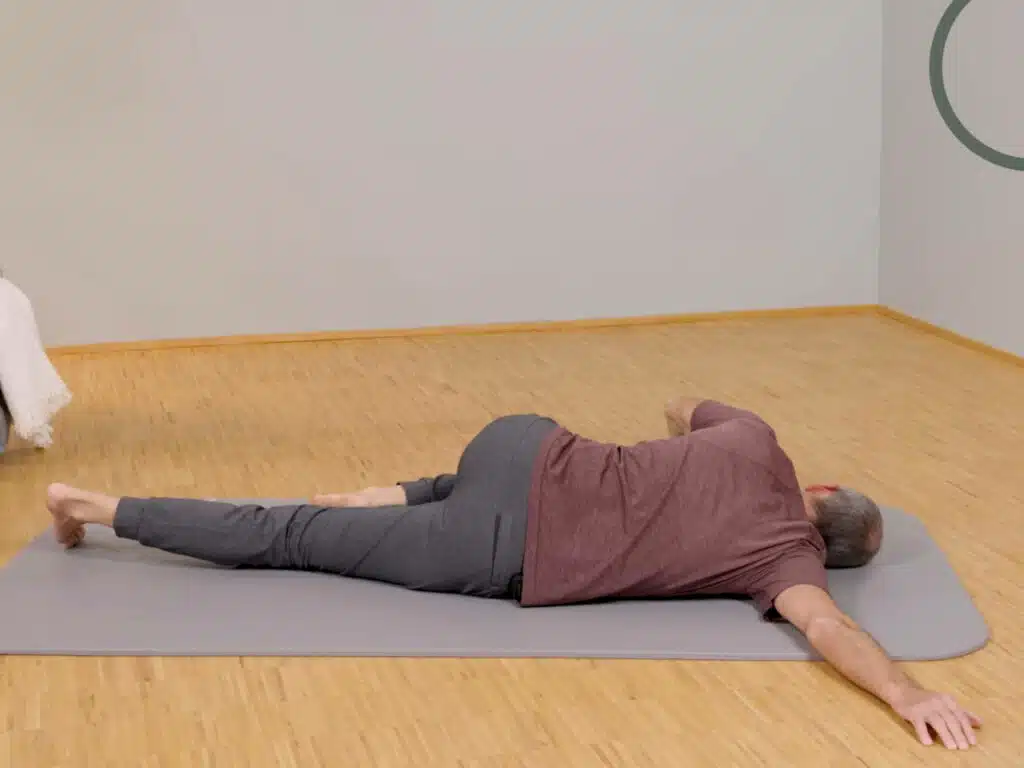 Roland Liebscher-Bracht liegt in Seitenlage auf dem Boden und hat einen Arm hinter sich gerade ausgestreckt.